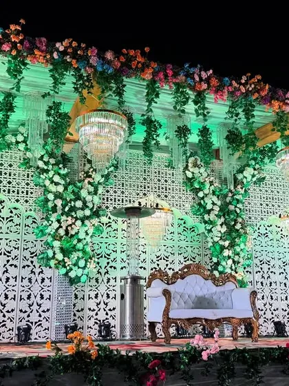 An angled shot of the white lattice wedding stage, showing the depth and detail of the floral work and the hanging crystal elements.