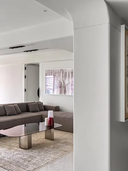 The informal living space in Apartment 56 is designed to be free and fluid. A monochromatic palette is punctuated by the bold crimson of a grand piano, creating a sophisticated yet relaxed atmosphere focused on art and natural light.