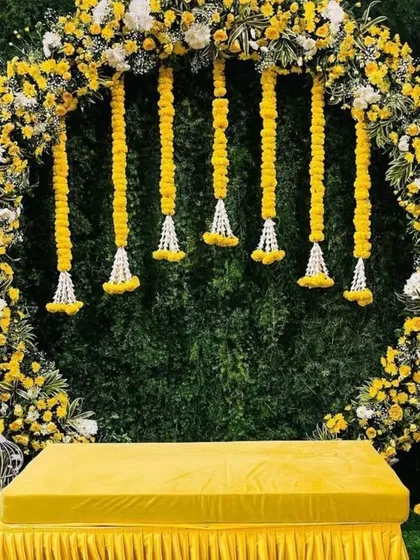 A modern take on Haldi decor is always so much fun. This setup features a full circular arch covered in yellow and white flowers against a lush green wall, creating a fresh and elegant backdrop for photos.