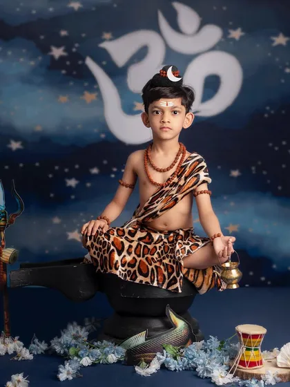 A young boy meditates peacefully as little Shiva, holding a brass kamandalu, with the sacred Om symbol glowing behind him.