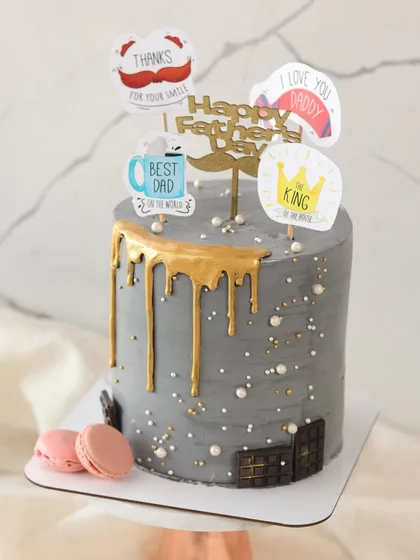 A modern grey drip cake for Father's Day, decorated with fun toppers like "King of the House" and "Best Dad."