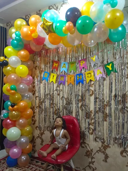A vibrant multicolor balloon arch against a silver shimmer curtain. This is a great example of a simple, budget-friendly yet very festive home birthday decoration.