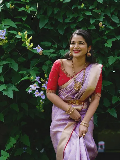 A client looking lovely in a lavender silk saree paired with a contrasting red blouse. The blouse features simple but elegant embroidery along the neckline.