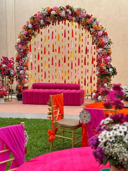 The main seating area for the Mehendi, featuring a floral arch with hanging tassels and a bright pink sofa.