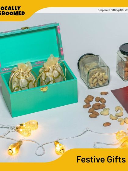 This festive gift set includes a decorative box filled with pouches of nuts and glass jars of treats, surrounded by festive lights. It's a perfect example of a warm and thoughtful holiday gift.