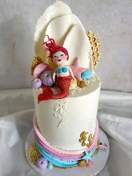 A mermaid theme cake with a beautiful, hand-sculpted mermaid sitting in a large white chocolate shell.
