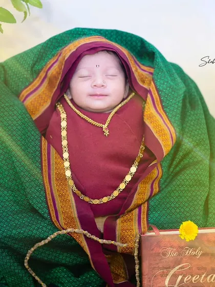 This sweet newborn Rakumai is posed with a holy book and a tulsi plant, creating a respectful and adorable portrait.
