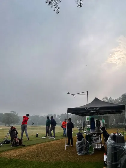 A golfer practices next to a demo tent on a foggy morning, showing dedication in any condition.