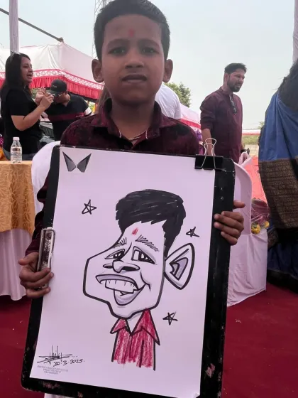 A young boy with his caricature at an outdoor event. The red carpet and tents suggest a large-scale festival or fair.