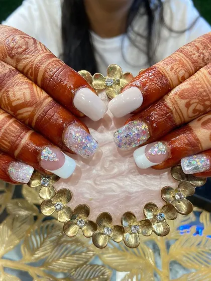 A full view of a gorgeous bridal nail set against the client's henna. The combination of white, glitter, and crystals is a timeless choice.