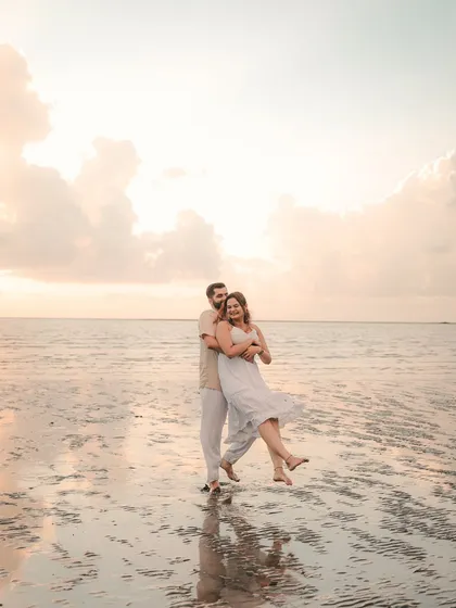 A playful and joyous moment on a Goan beach, with the groom lifting the bride as the waves reflect the soft sky. This captures the fun, relaxed vibe of a coastal pre-wedding shoot.