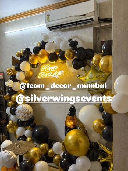 A full circular balloon arch in black, gold, and white, creating a fantastic photo booth for a birthday party at home. The neon sign adds a modern touch.