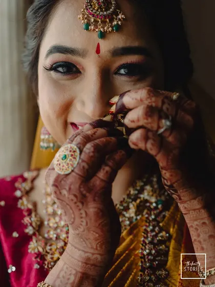 A close-up of the bride adjusting her nose ring, her smile hinting at her joyful anticipation. The shot highlights her beautiful henna and traditional ring.