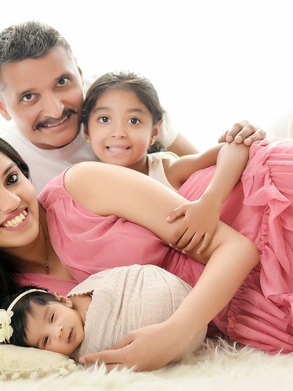 A happy family of four, including a newborn and an older sister, posing together on a soft rug. This image captures the complete family unit, full of love and connection.