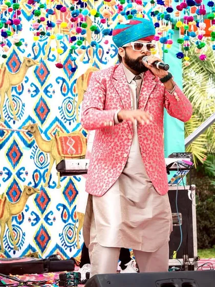 The lead singer of a fusion band performing on a stage with a camel-print backdrop, perfectly matching the Rajasthani carnival theme.
