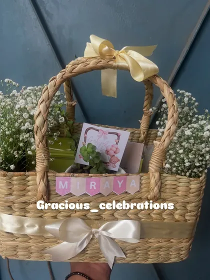 This beautiful cane basket was part of a 250-piece order for a first birthday. It's filled with a cake loaf, organic honey, cookies, a jade planter, and a scented candle, all decorated with fresh flowers.