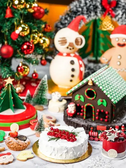 A festive table filled with an array of Christmas desserts, including cakes, cookies, and chocolate figures. This shot showcases the breadth of a bakery's holiday collection.