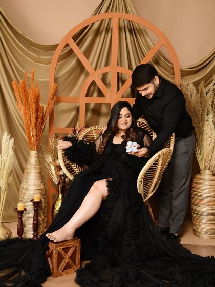 A sweet moment between the expecting couple in our boho-chic setup. The partner presents a pair of tiny baby shoes, adding a personal and emotional touch to the shot.