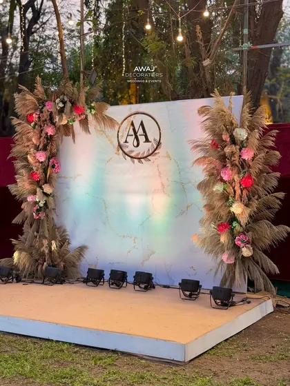A beautiful boho-chic stage for an outdoor sangeet, with pampas grass arches, a marble-effect backdrop, and a custom monogram.