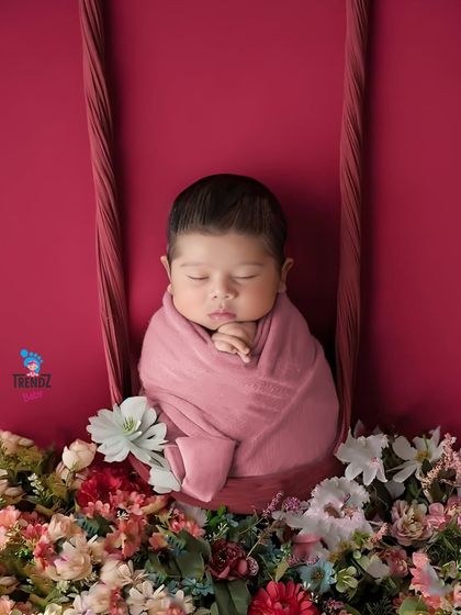 A newborn rests peacefully on a floral swing prop. The rich red background and soft flowers create a warm and romantic setting for this beautiful shot.