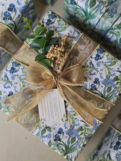 A close-up of the gold ribbon detailing. The pearl-edged organza ribbon, paired with the custom floral paper and dried wheat, creates a look of rustic luxury.