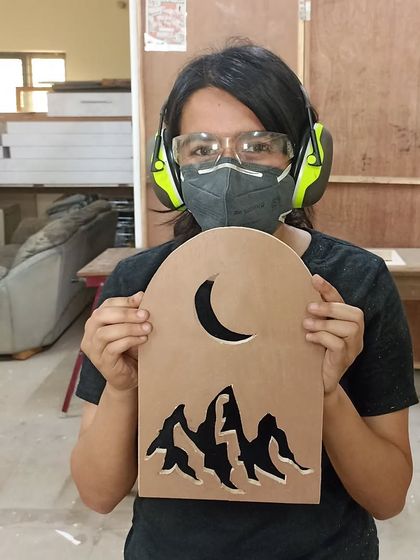 A student proudly displays a mountain-and-moon scene he cut out of MDF using a jigsaw. This shows the artistic possibilities of a tool often used for simple cuts.