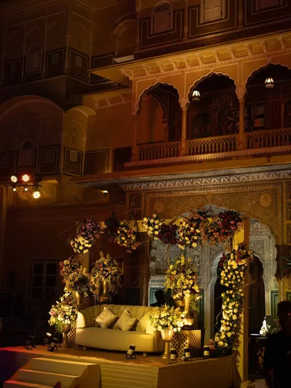 The stage seating for the Sangeet, framed by floral arrangements against the beautifully lit, historic walls of the palace.