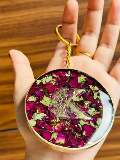 A beautiful handmade resin keychain featuring a gold initial 'K' surrounded by dried rose petals. Each piece is unique and handcrafted with care.