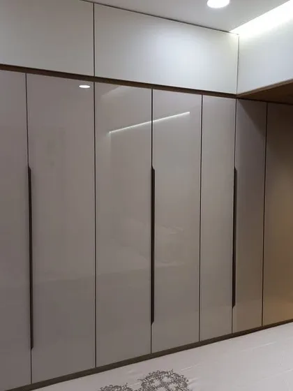 A floor-to-ceiling hinged wardrobe with a high-gloss beige finish and long, modern black handles. This design offers a sleek and expansive storage solution that blends seamlessly with the bedroom wall.