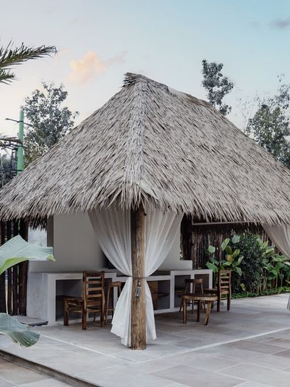 The outdoor gazebo, with its thatched roof and flowing white curtains, offers a shaded retreat by the pool. It’s an ideal spot for outdoor dining or lounging, fully embracing the tropical resort lifestyle.