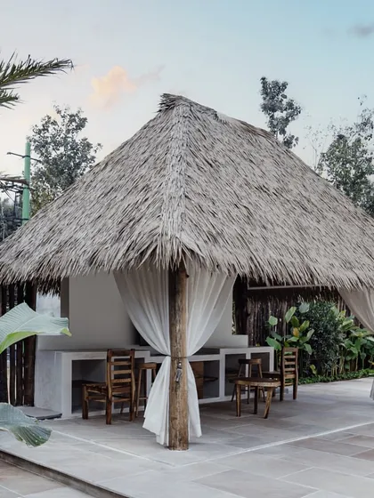 A close-up of the poolside cabana, featuring a traditional thatched roof and flowing white curtains. This simple structure provides a shaded, breezy spot for relaxation, embodying the essence of a tropical getaway.