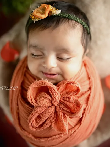 A close-up of a smiling newborn wrapped in a rust-colored swaddle. The warmth of the color and the baby's joyful expression make this an incredibly heartwarming portrait.