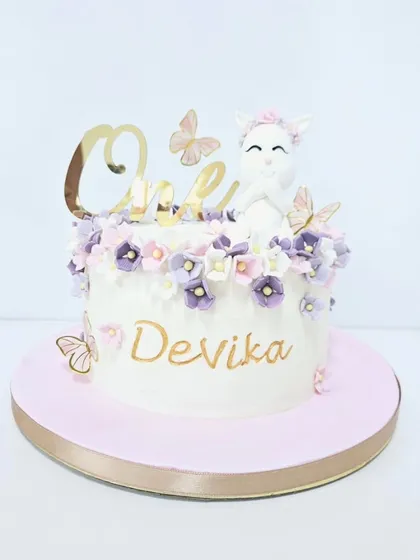 A sweet and simple cake for a first birthday. This design features a cute, handcrafted kitten topper surrounded by delicate pastel flowers and butterflies, with a golden "One" to mark the special milestone.