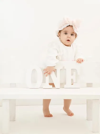 A clean and classic all-white setup for a first birthday. This little girl standing by the "ONE" letters is the picture of sweetness.
