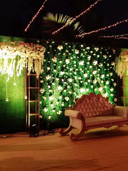 We created this luxurious reception stage with a full wall of artificial greenery and white roses. The design includes cascading floral chandeliers and elegant seating, providing a lush and sophisticated photo backdrop for the couple.