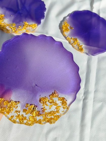 A close-up view of one of the purple and gold resin coasters, highlighting the vibrant color and the texture of the gold leaf detailing.