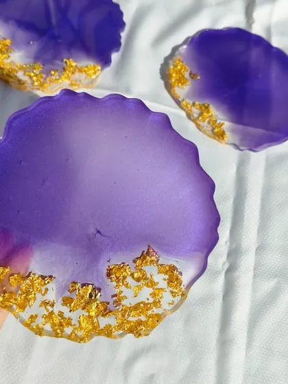 A close-up view of one of the purple and gold resin coasters, highlighting the vibrant color and the texture of the gold leaf detailing.