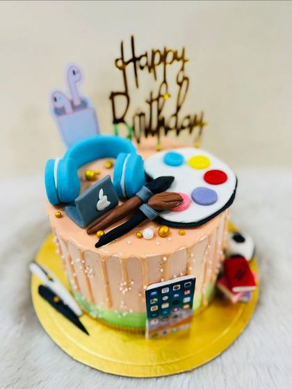 An artist's dream cake, decorated with fondant headphones, a laptop, an iPhone, paintbrushes, and a color palette.