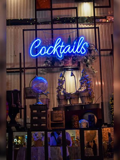 A 'Cocktails' neon sign integrated into a modern, industrial-style shelving unit. This setup is perfect for contemporary venues, blending seamlessly with urban decor while adding a pop of color.