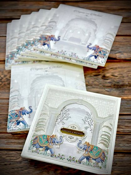 A trending and royal hardback wedding invite that captures the essence of a palace wedding. The design features beautifully illustrated elephants against a backdrop of intricate architecture, finished with a metallic nameplate.