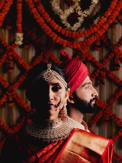 A creative and dramatic couple portrait against a backdrop of red floral decor. The use of shadow and light on the bride's face creates a powerful, artistic image that feels both traditional and modern.