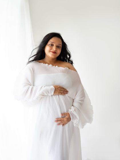 A beautiful, happy portrait of the mom-to-be looking directly at the camera with a warm smile. The flowing white gown and natural light give her an amazing glow.