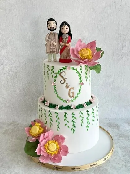 A sweet and personal engagement cake for a lovely couple. This design features hand-painted vines, a custom monogram, and beautiful handmade lotus sugar flowers, all topped with figurines that look just like the happy couple.