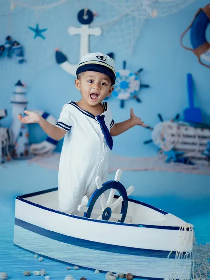 All aboard for a nautical adventure. This toddler portrait showcases one of our popular themes, featuring a sailor outfit, a boat prop, and a backdrop that sets the stage for imaginative play and adorable photos.