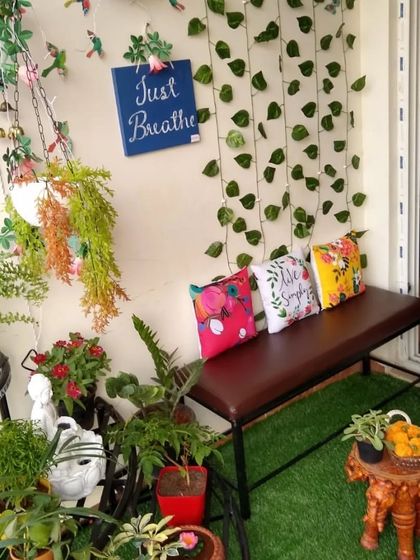 A colourful and lively balcony corner filled with plants and personality. It features a comfortable bench with bright cushions, hanging planters, and a 'Just Breathe' sign, reminding you to relax and enjoy your green space.