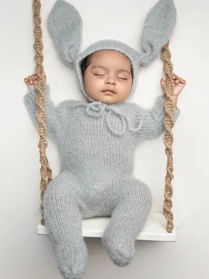 Our "posed and dreamy" sessions are all about creating adorable, artistic portraits. This little one is sleeping so peacefully in our popular hand-knitted bunny costume, perched on a custom-made swing prop. It's a perfect example of the gentle, styled newborn photography we love to create.
