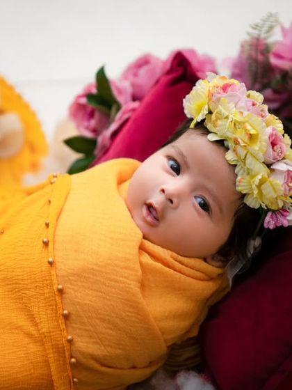 An awake newborn with bright eyes is swaddled in a beautiful yellow drape, wearing a floral crown. We are experienced in capturing both sleeping and awake babies, showcasing their curious and alert expressions.