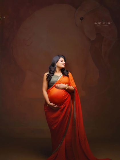 A standing portrait that emphasizes the beauty of the baby bump under the saree. The elephant motif in the background adds a symbolic touch.