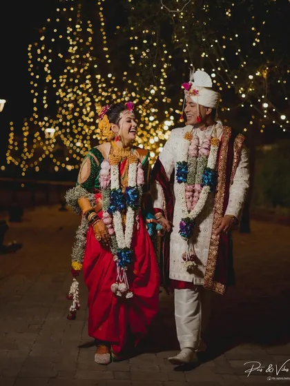 Walking hand-in-hand under a canopy of twinkling lights. This candid shot captures the pure laughter and joy of a newly married Maharashtrian couple.