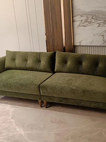 This deep olive green sofa features subtle button-tufting on its back cushions, adding a touch of classic detail to its modern form. The plush velvet fabric makes it an exceptionally comfortable and inviting piece.